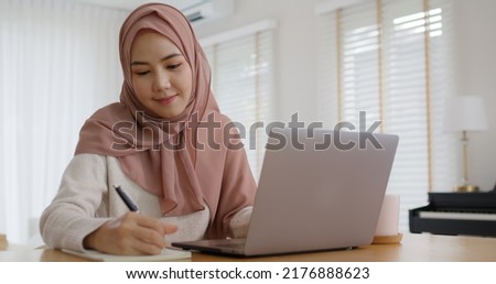 Young Gen Z workforce islam woman self learn MBA online class reskill upskill job at home. Asia people arab girl study relax sit at table wear hijab scarf write or typing e-mail work on digital laptop