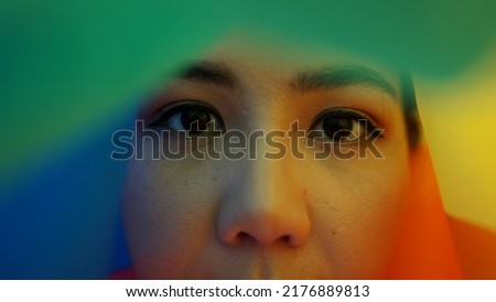 Portrait young teen queer transgender asia people look at camera under colorful stripes flag. Closeup eye face cry sad hiding true self identity in gay LGBT LGBTQIA bisexual mental illness problem.  Royalty-Free Stock Photo #2176889813