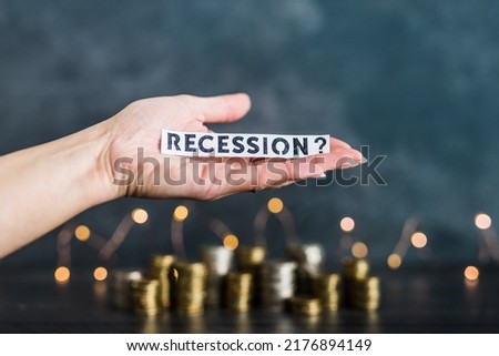 recession and inflation after the Covid-19 pandemic conceptual image, hand holding Recession text in front of stacks of coins with fairy lights in the background Royalty-Free Stock Photo #2176894149