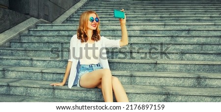 Happy smiling young woman taking selfie with smartphone sitting on the stairs on city street background