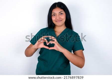 Serious Doctor hispanic woman wearing surgeon uniform over white background keeps hands crossed stands in thoughtful pose concentrated somewhere