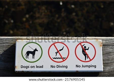 Corroding white sign on a pier informing people that dogs must be on a lead, and that no jumping or diving into the water is permitted