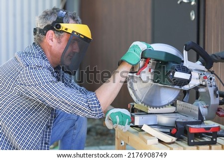 a handyman in a protective helmet works with a miter saw Royalty-Free Stock Photo #2176908749