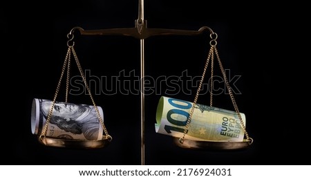 Banknotes of 100 US dollars and 100 euros on scales Royalty-Free Stock Photo #2176924031