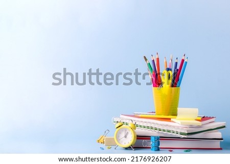 Many different various school, office supplies and stationery. Back to school concept. Notebook, book, pen, pencil, scissors, alarm clock, clock, sticker stand on a wooden table on a green background.