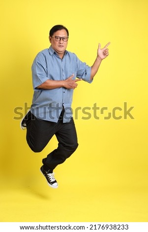 The adult Asian man with blue shirt standing on the yellow background.