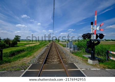 Guarded railroad crossing with open barriers, red warning light and cross of Saint Andrew in the NEtherlands. Royalty-Free Stock Photo #2176942955