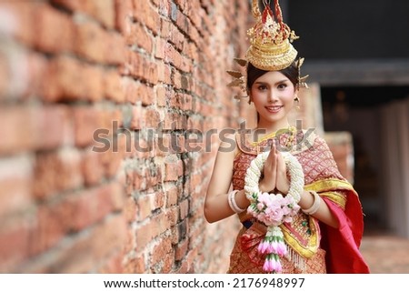 Happy smiling young fashion and beautiful asian woman in Thai traditional costume pay respect sawasdee symbol with jasmine flower garland in ancient buddha temple Ayutthaya, Thailand. Travel concept Royalty-Free Stock Photo #2176948997