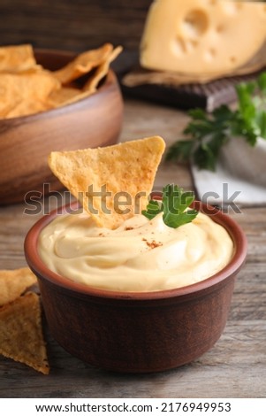 Delicious cheese sauce with nacho and parsley on wooden table Royalty-Free Stock Photo #2176949953