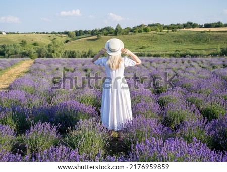 woman model in white dress outfit with hat is standing dancing in lavender field, photo session 