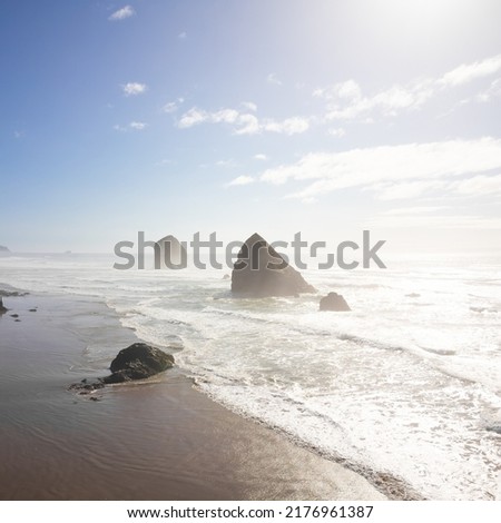 Long sandy shore of the ocean. There are big boulders in the water. There are light white clouds in the light blue sky. There are no people in the photo. Calm scenes. Recreation, tourism, ecology.