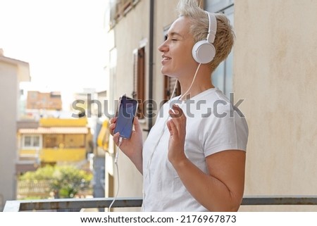 Middle Aged Woman With Short Haircut Listening To Music With Her Smartphone. Audiobook or Podcast Concept. Active Life Position. Wired On-Ear Headphones