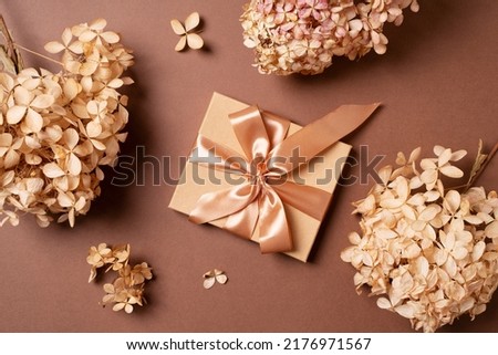 Gift box with golden ribbon and dry grass and flowers on brown background flat lay, top view, copy space Royalty-Free Stock Photo #2176971567