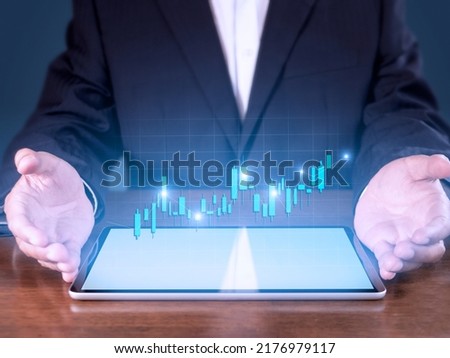 Hand of businessman present tablet analysis stock market graph growth and increase of chart positive indicators. Hand holding tablet show stock chart on blue background.