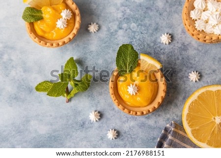 Mini tarts with lemon curd, mini meringue, lemon slices and mint on blue concrete background. Top view.