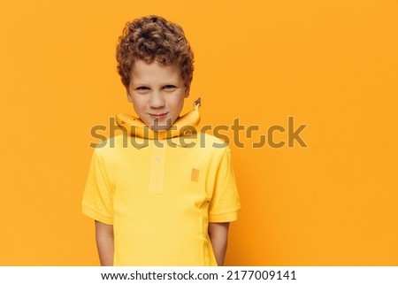 a cute, funny boy with curly hair stands on a yellow background in yellow clothes and holds a banana with his neck