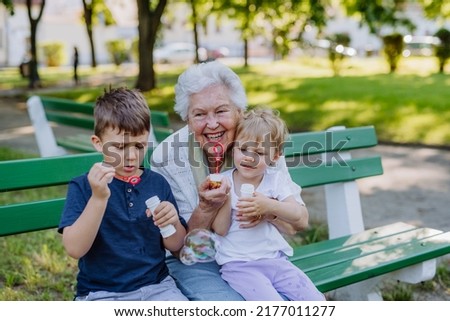 Great grandmother sitting on bench with her grandchildren and blowing soap bubbles together, generation family concept. Royalty-Free Stock Photo #2177011277