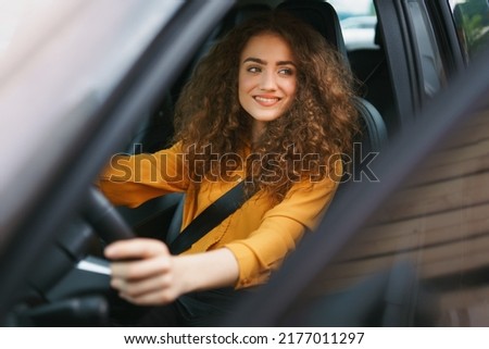Young woman driving a car in the city. Portrait of a beautiful woman in a car, looking out of the window and smiling. Royalty-Free Stock Photo #2177011297