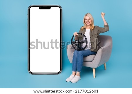 Photo of aged lady sit chair hold steering wheel fist up gadget app discounts poster isolated blue color background