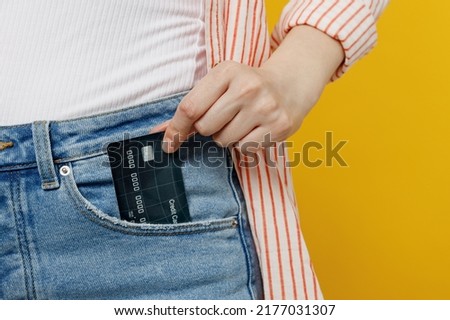 Cropped photo shot close up woman she wears striped shirt white t-shirt hold put into pocket mock up of credit bank card isolated on plain yellow background studio portrait. People lifestyle concept