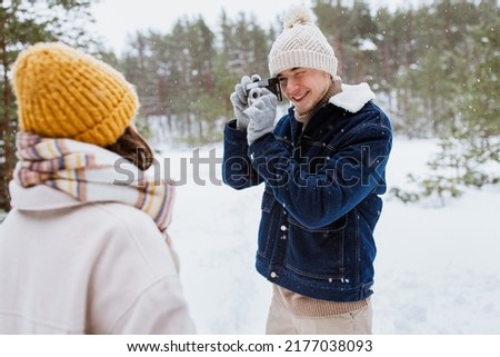 people, love and leisure concept - happy smiling man photographing woman in winter forest