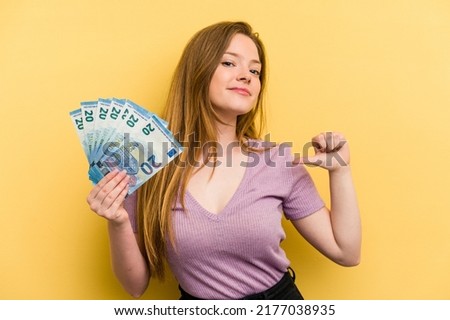 Young caucasian woman holding banknotes isolated on yellow background feels proud and self confident, example to follow.