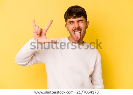Young caucasian man isolated on yellow background showing a horns gesture as a revolution concept.