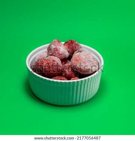 frozen strawberries in a small white bowl on a green background