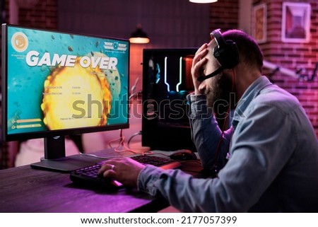 Sad male streamer losing action video games championship with multiple players on internet. Modern gamer streaming gameplay and feeling frustrated about lost gaming tournament. Royalty-Free Stock Photo #2177057399