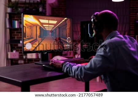 Content creator having fun with video games play competition, using computer to stream online championship. Male gamer playing rpg action tournament game at desk with neon lights. Royalty-Free Stock Photo #2177057489