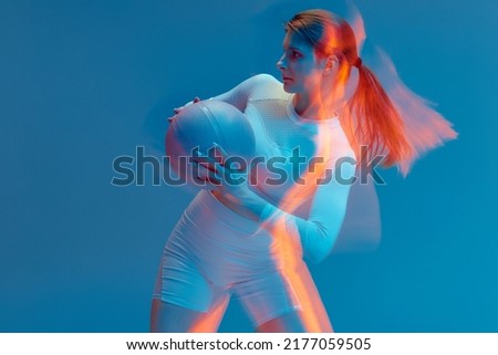 Sporty beautiful girl in white tracksuit on blue background turning with the ball . Isolated figure with light painting effect