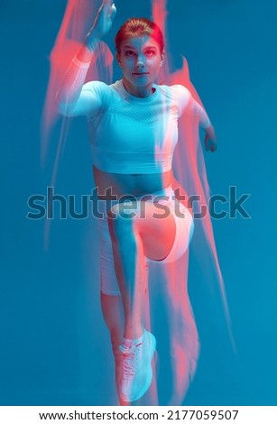 Girl running in white sport suit on blue background. Isolated sport model in studio with light painting effect.