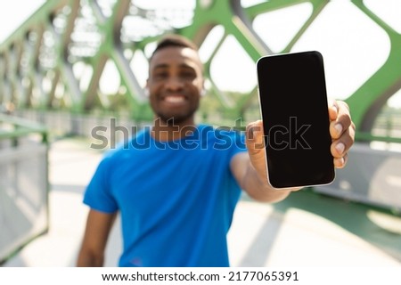 Portrait of a dark-skinned guy holding a large smartphone in his hand with a blank screen, for a mockup, a banner