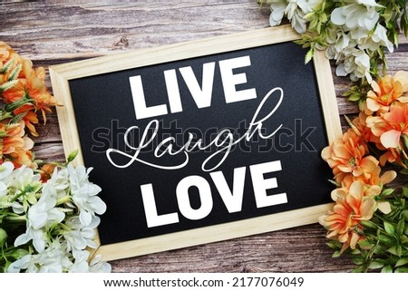 Live Laugh Love typography text written on wooden blackboard with flower bouquet decorate on wooden background