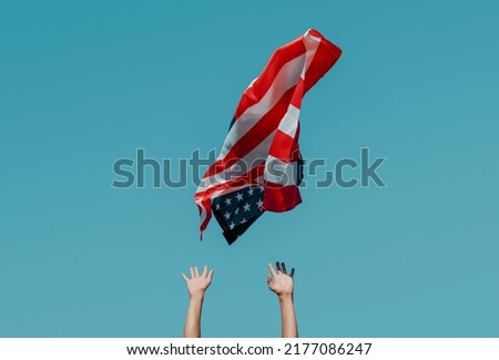a caucasian man is propelling a flag of the United States to the blue sky, or is about to catch it as it is flying in the air