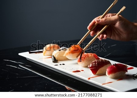 Hand holding bamboo chopsticks a elegant piece of sushi while soaking it in soy sauce at restaurant. Front view. Japanese cuisine concept. Royalty-Free Stock Photo #2177088271