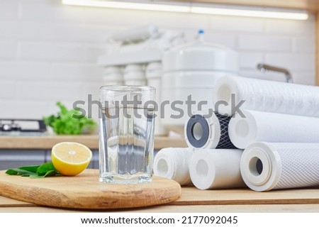 Glass of filtered clean water with reverse osmosis filter, lemons and cartridges on a table in kitchen. Concept Household filtration or purification system. Royalty-Free Stock Photo #2177092045
