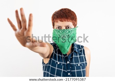 a mid age Latin woman covers her face with a scarf and shows her hand in a stop sign
