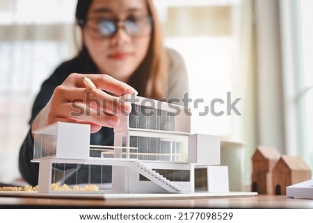 Undergraduate architecture students work on models of the modern box house. Holding the part of the model while thinking about concepts of building and construction. Focusing on her hand. Royalty-Free Stock Photo #2177098529