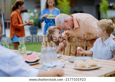 Multi generation family having garden party celebration, grandfather is entertaining grandchildren, laughing and having fun. Royalty-Free Stock Photo #2177101923