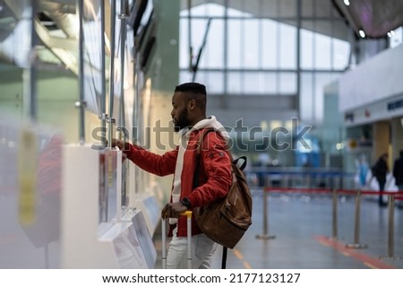 African young man traveler showing documents and boarding pass at check-in counter in airport, travelling with luggage. Male passenger giving passport to officer at border control. Tourism, air travel Royalty-Free Stock Photo #2177123127