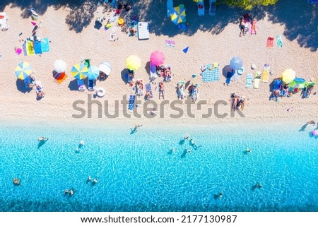 Aerial view on beach, pepole and umbrellas. Vacation and adventure. Beach and blue water. Top view from drone at beach and azure sea. View on the coast from drone. 