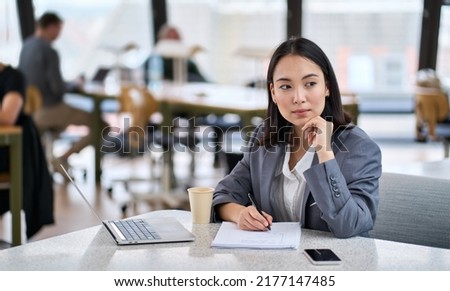 Young thoughtful Asian business woman executive manager wearing suit working in modern office, taking notes and thinking of professional plan, project management, considering new business ideas. Royalty-Free Stock Photo #2177147485