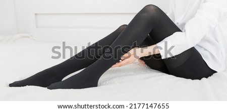 Beautiful woman putting on stocking indoors, closeup. Beautiful long female legs in stockings. Girl putting on stockings at home in a white room. Black tights.
