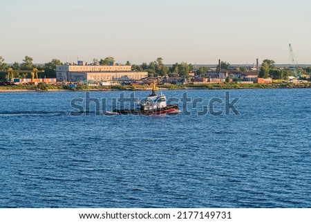 a tugboat sails along the wide river Severnaya Dvina northern part of Russia against the background of industrial structures on the shore. copy space.