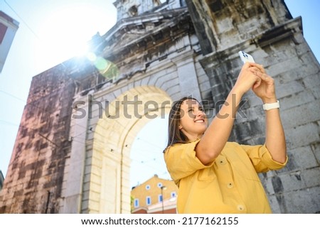 Lifestyle portrait of happy foreign woman tourist taking photo with smartphone during sightseeing in old town of Lisbon, Portugal. Female traveler making photo content from journey