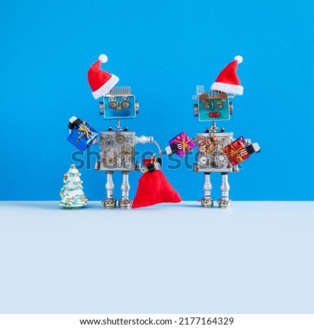 A pair of toy mechanical robots Santa Clauses are holding gifts and posing near a small Christmas tree. Mock up blank for Christmas New Year greeting card or poster. blue gray background, copy space
