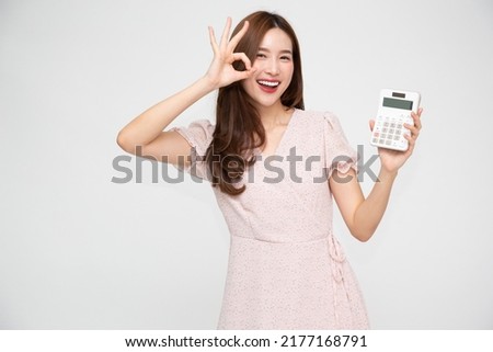 Portrait of excited young Asian woman holding calculator and showing OK sign isolated on white background, Business and financial concept