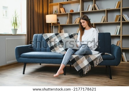 Portrait of a young happy female freelancer sitting on the couch and working on project, watching movie on laptop, studying, blogging, resting and chatting online. High quality photo. Royalty-Free Stock Photo #2177178621