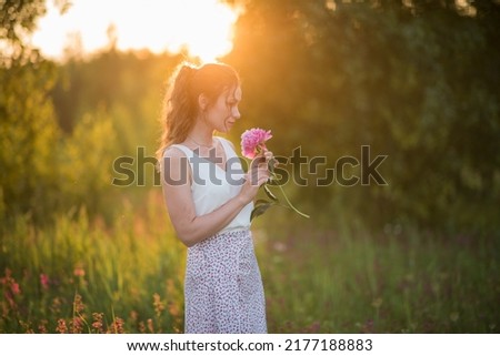Beautiful happy young girl with peonies in nature outdoors in the sun. Beautiful woman in a field with flowers in a long skirt. High quality photo